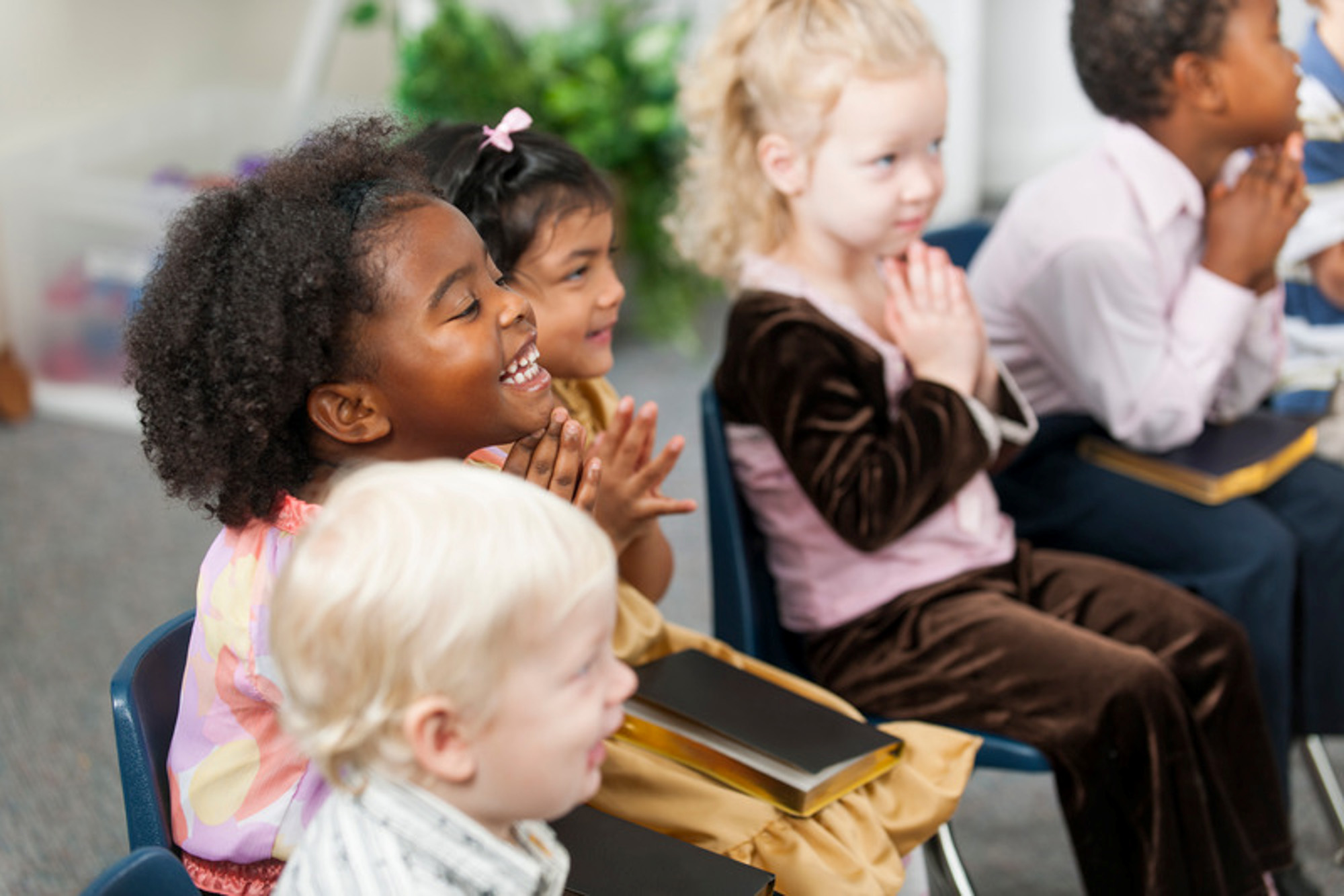 Children in chairs clapping together.