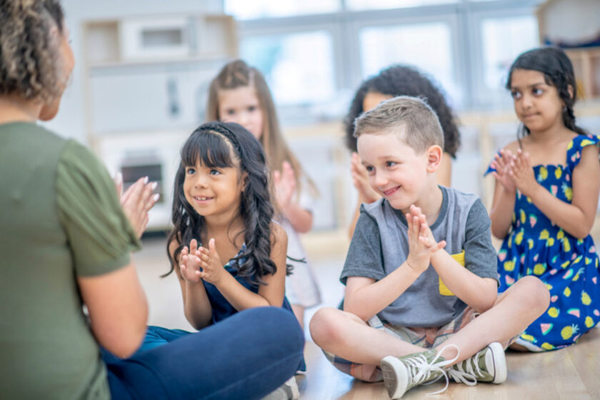 Children sitting together in a group and clapping.